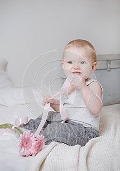 Blonde girl sitting on a bed with pink flowers and ribbon, portrait of a cute baby