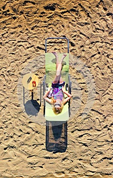 Blonde girl sitting on a chair on the beach. Top view