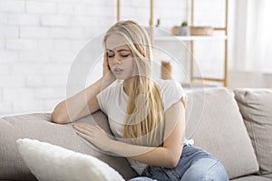 Blonde girl sitting on sofa, suffering from migrane