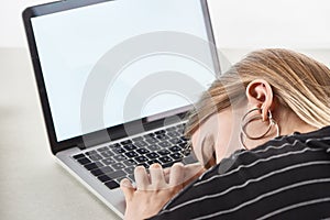 Blonde girl sleeping near laptop with blank screen, cyberbullying concept.