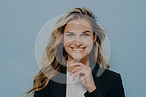 Blonde girl smiling at camera with hand next to her chin