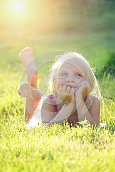 Blonde girl smiling and lying on the grass at summer sunset looking at the sky. Natural happiness, fun and harmony