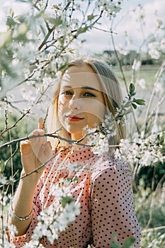 Blonde girl on a spring walk in the garden with cherry blossoms. Female portrait, close-up. A girl in a pink polka dot