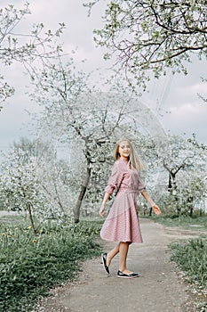 Blonde girl on a spring walk in the garden with cherry blossoms. Female portrait, close-up. A girl in a pink polka dot