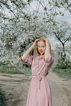 Blonde girl on a spring walk in the garden with cherry blossoms. Female portrait, close-up. A girl in a pink polka dot