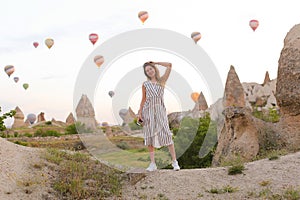 Blonde girl standing with many hot air balloons on background in Capadocia, Turkey.