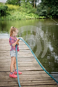 A blonde girl stands on a wooden pier on the river bank.