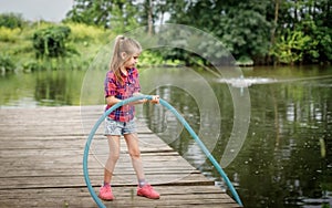 A blonde girl stands on a wooden pier on the river bank.