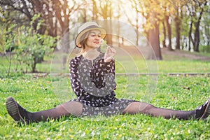 Blonde girl in a straw hat with a dandelion in his hand lies  on the grass in the spring garden.