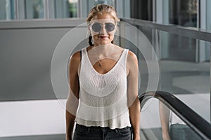 Blonde girl with sunglasses climbing an escalator