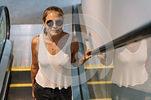 Blonde girl with sunglasses climbing an escalator