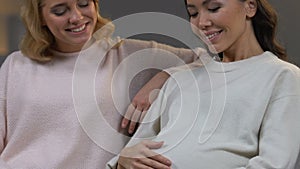 Blonde girl supporting her pregnant asian friend, women smiling enjoying pastime