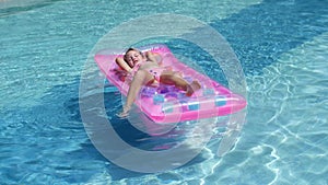 Blonde girl swims in the pool on an inflatable mattress