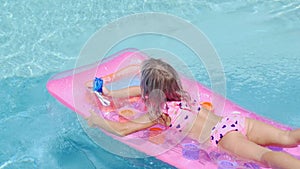 Blonde girl swims in the pool on an inflatable mattress