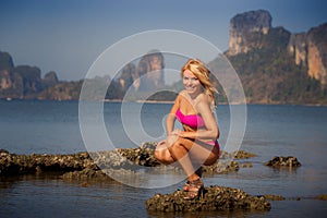 blonde girl in swimsuit smoothes hair on stone