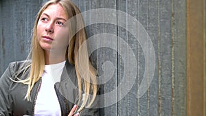 Blonde girl teenager young woman looking sad or thoughtful wearing a green jacket in an urban city environment