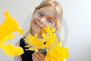 A blonde girl of ten years holds a bouquet of yellow daffodils in her hands, close-up, bokeh