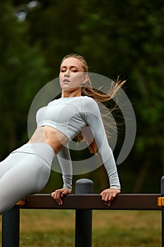 A blonde girl in a tracksuit trains in a park in an urban landscape, a cross-fit instructor doing exercises from yoga