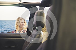 Blonde girl traveler outside a car off road with ocean behind