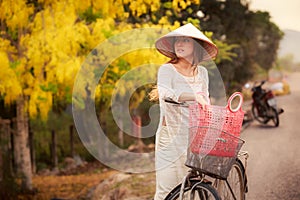 blonde girl in Vietnamese and hat by bike against yellow plant