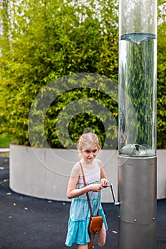 Blonde girl in white and blue dress playing in the playground in the summer park of entertainments