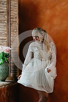 A blonde girl in white dress dancing by the window, flowers