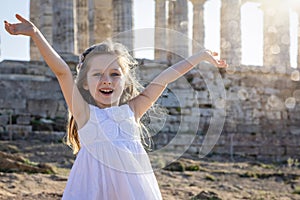 A blonde girl in a white summer dress in front of an ancient, Greek temple