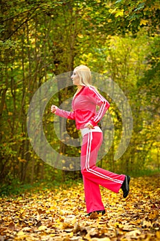 Blonde girl young woman running jogging in autumn fall forest park