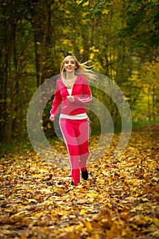 Blonde girl young woman running jogging in autumn fall forest park