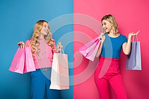 Blonde girls with shopping bags looking at each other on pink and blue background
