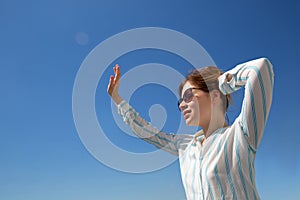 Blonde with glasses waving hand to someone against the blue sky