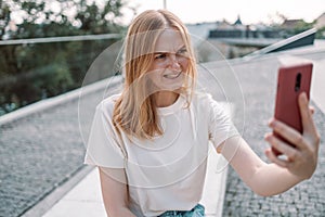 Blonde hair angry young woman posing outdoors in park take a selfie by mobile phone while standing in the park.