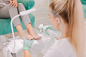 Blonde-haired chiropodist spraying some sanitizer on feet of client