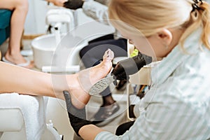 Blonde-haired chiropodist using instruments making manicure photo