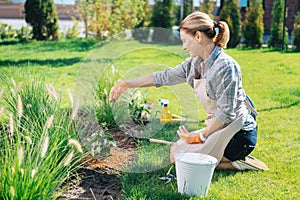 Blonde-haired family woman sitting on the grass near little hoe enriching soil