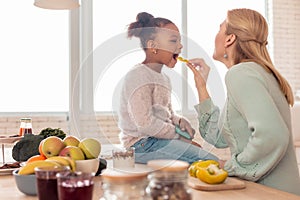 Blonde-haired mother feeding her cute funny girl with fruits