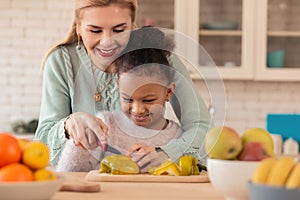 Blonde-haired mother teaching her daughter cutting vegetables