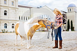 Blonde-haired smiling cowboy girl feeding her little pony