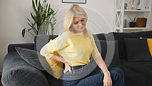 Blonde-haired woman felt a sharp pain in loin sitting on the sofa at home