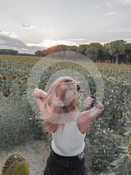 Blonde-haired woman in sunflower field at sunset touching her hair