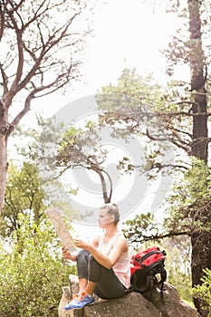 Blonde hiker sitting on rock and reading map