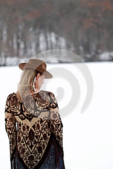 Blonde hippy woman with fringed patterned bohemian poncho outdoors in snow with wearing cowboy hat with feathers Stevie Nicks vibe