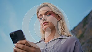 Blonde lady texting mobile phone at blue sky. Serious woman looking smartphone