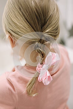 Blonde little girl braid hair with pink ribbon bow. Haircare, hairstyling.