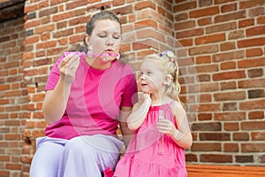 Blonde little girl with cochlear implant blowing soap bubbles with her mother outdoor. Hear impairment deaf and health