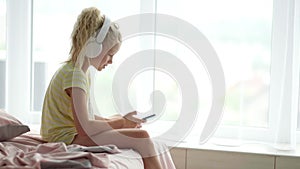 Blonde little girl kid in headphones with phone in hands. child listening enjoying music. rest, relaxation, quiet time