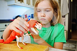 A blonde little girl makes a dinosaur craft out of wood and air plasticine.