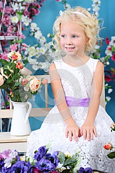 Blonde little girl in white dress sits on bench