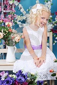 Blonde little girl in white dress sits on bench