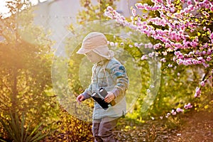 Blonde little toddler child with binoculars, sitting in garden on sunset